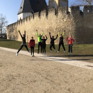 Läufergruppe der Rückenwind Fitnessschule springt vor der historischen Stadtmauer bei den Laufkursen in der Nähe von Ingelheim